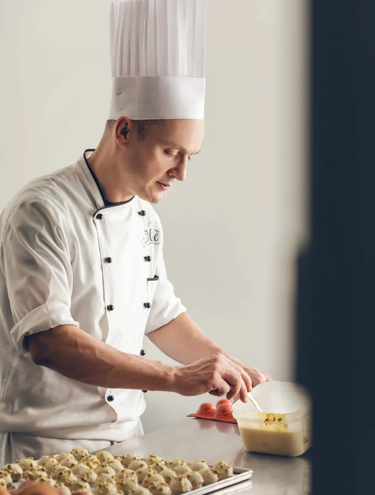 Pasticcere in divisa bianca che rifinisce un vassoio di dolci